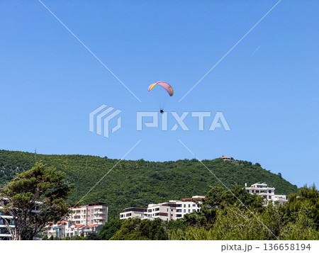 A paraglider flying high in the clear blue sky above the horizon. Freedom, adventure and extreme recreation in open aerial space. 136658194