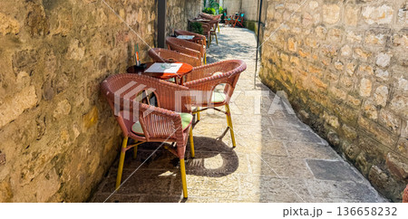 Outdoor cafe chairs along a narrow stone alley banner with copy space. Travel, leisure, lifestyle and relaxation in a historic European setting. 136658232