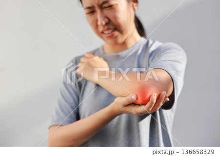 Young woman suffering from acute elbow pain and joint inflammation with red highlight effect, female touching sore arm, tendonitis, sports injury, arthritis, health problem, copy space background. Young woman suffering from acute elbow pain and joint inflammation with red highlight effect, female touching sore arm, tendonitis, sports injury, arthritis, health problem, copy space background. 136658329