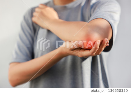 Young woman suffering from acute elbow pain and joint inflammation with red highlight effect, female touching sore arm, tendonitis, sports injury, arthritis, health problem, copy space background. 136658330