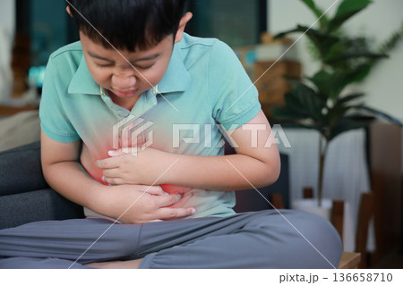 Asian boy holding belly suffering from severe abdominal pain with red inflamed area. Concept of stomach ache, indigestion, food poisoning, gastritis, and pediatric medical healthcare treatment. Asian boy holding belly suffering from severe abdominal pain with red inflamed area. Concept of stomach ache, indigestion, food poisoning, gastritis, and pediatric medical healthcare treatment. 136658710