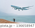 Flight trip to Phuket in Thailand during the rainy season. A plane flying low over the sea lands at the airport on the island, a vacationing tourist with an umbrella on the beach meets and photographs 136658947
