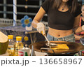A woman flips roti on a hot pan at a street market in Bangkok. She wears gloves and focuses on preparing this traditional Thai snack for customers enjoying local food. High quality photo 136658967