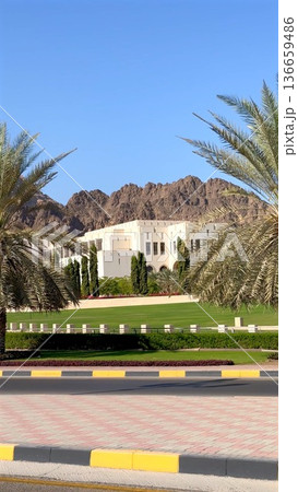 Resort Facade Glimpsed Behind Row Of Palms And Manicured Lawn, Low Stone Fence, Colorful Planters And Rugged Mountains Offering Polished Hospitality Entrance Impression Resort Facade Glimpsed Behind Row Of Palms And Manicured Lawn, Low Stone Fence, Colorful Planters And Rugged Mountains Offering Polished Hospitality Entrance Impression 136659486