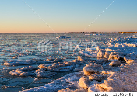 Frozen Baltic Sea Coast at Sunset with Ice Floes and Glowing Winter Light in Latvia, Liepaja 136659493