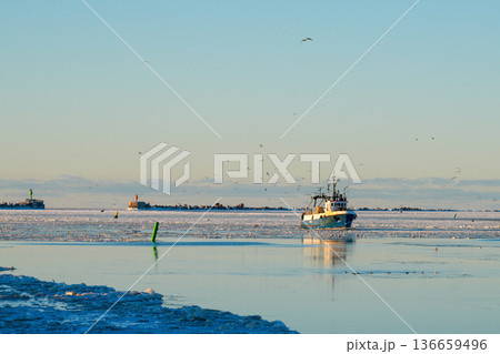 Fishing Vessel Returning to Liepaja Port Through Frozen Baltic Sea at Winter Sunset Fishing Vessel Returning to Liepaja Port Through Frozen Baltic Sea at Winter Sunset 136659496