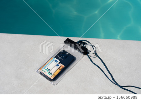 Waterproof pouch protecting smartphone and euro banknotes on a poolside, ensuring safety and security for valuables during summer vacation 136660989