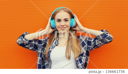 happy young woman listening to music with headphones on orange background happy young woman listening to music with headphones on orange background 136661736