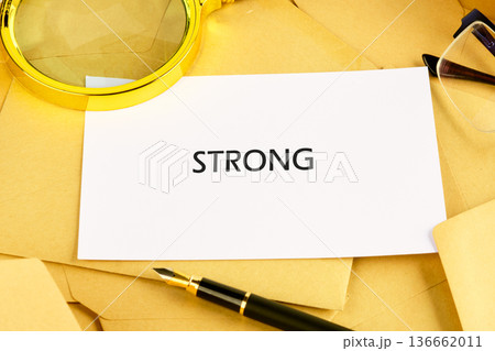 A striking word STRONG appears on a pristine white card, set on golden envelopes 136662011
