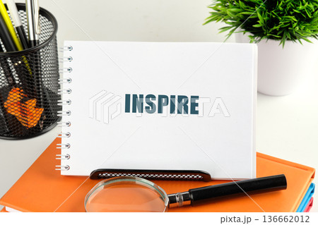 INSPIRE notebook on a desk with pens, books, green plant. Magnifying glass for detail INSPIRE notebook on a desk with pens, books, green plant. Magnifying glass for detail 136662012