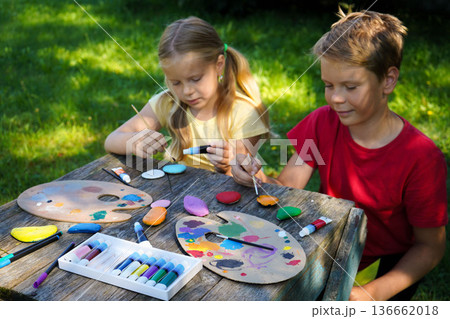 Using vibrant acrylics, children transform smooth, flat stones into colorful canvases for their imagination, creating perfect handmade gifts. 136662018