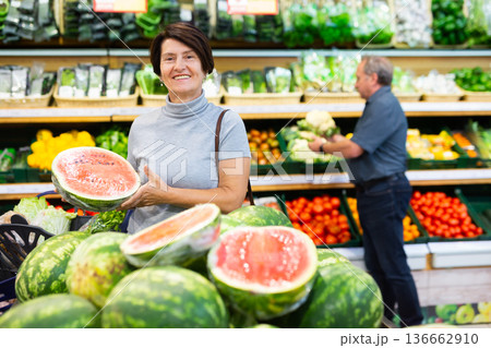 elderly woman chooses watermelon in fruit and vegetable section 136662910