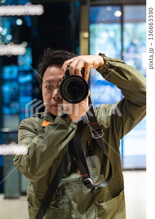 A photographer holds a camera and looks through the lens inside an indoor space. The image represents professional photography and visual content creation. 136663390