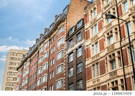 Classic British architecture lines a traditional London street, with red brick buildings and historic facades beneath a cloudy sky. 136663409