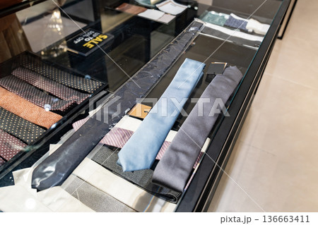 A customer compares two neckties on a glass counter inside a clothing store. The scene supports content about buying decisions and retail fashion choice. 136663411