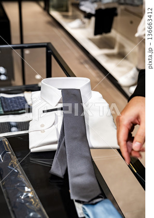 A customer compares two neckties on a glass counter inside a clothing store. The scene supports content about buying decisions and retail fashion choice. 136663412