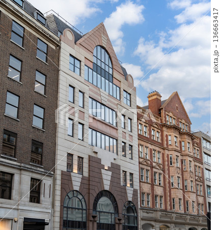 Classic British architecture lines a traditional London street, with red brick buildings and historic facades beneath a cloudy sky. 136663417