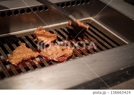 Beef slices cook on a metal grill with visible heat and browning surface, reflecting a professional restaurant environment and active food preparation process. 136663424