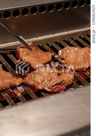 Beef slices cook on a metal grill with visible heat and browning surface, reflecting a professional restaurant environment and active food preparation process. Beef slices cook on a metal grill with visible heat and browning surface, reflecting a professional restaurant environment and active food preparation process. 136663425