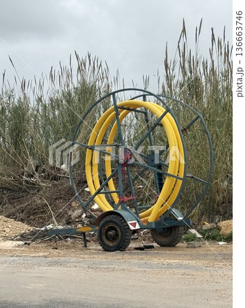 Agricultural irrigation equipment with yellow hose reel, standing on a rural road background 136663746