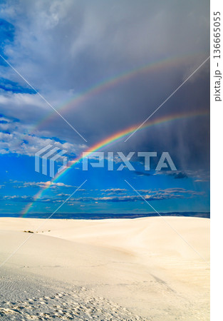 White Sands National Park in New Mexico. Scenic landscape features a colorful double rainbow arching over white gypsum sand dunes under a dramatic stormy sky 136665055
