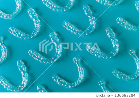 Clear dental aligners arranged on a blue background, showcasing their transparent design and unique shape for orthodontic treatment and teeth straightening 136665284