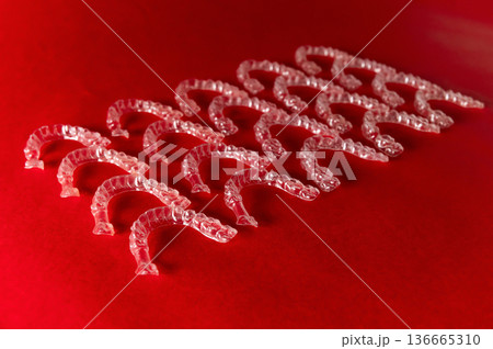 Clear plastic dental aligners arranged in a neat row on a vibrant red background, showcasing their transparent design and unique shape for orthodontic treatment Clear plastic dental aligners arranged in a neat row on a vibrant red background, showcasing their transparent design and unique shape for orthodontic treatment 136665310