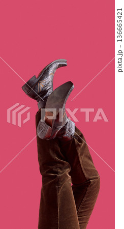 Female legs in brown cowboy boots and corduroy pants raised on pink background. 136665421