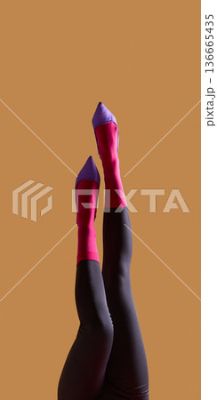 Female legs in pink socks and purple heels raised on beige background. Female legs in pink socks and purple heels raised on beige background. 136665435