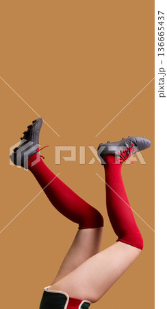 Female legs in red knee socks and black cleats raised on beige background. 136665437
