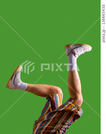 Male legs in white sneakers and striped shorts playful pose on green background. 136665438