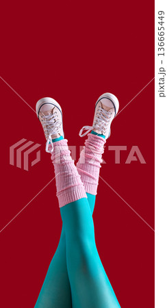 Raised legs in beige sneakers with pink leg warmers and turquoise tights on red background 136665449
