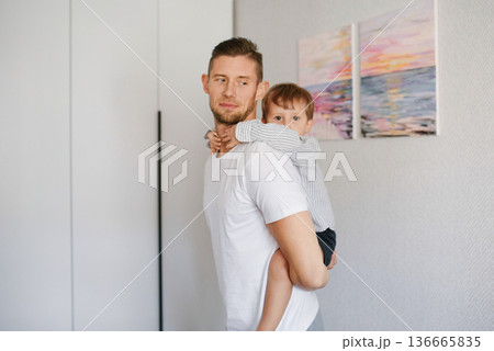 Father Carrying Young Son In Bright Modern Room Father Carrying Young Son In Bright Modern Room 136665835