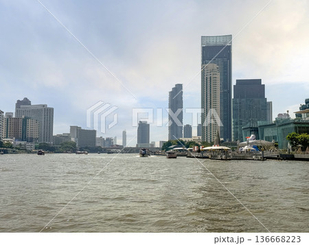 Scenic view of the Chao Phraya River in Bangkok with reflections of tall buildings and boats cruising along the water captured from the center in 2024 136668223