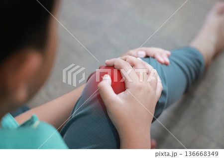 Asian boy showing painful face expression holding red inflamed knee from joint injury or accident. Pediatric healthcare concept of childhood bone problems, growth pain, and orthopedic treatment. Asian boy showing painful face expression holding red inflamed knee from joint injury or accident. Pediatric healthcare concept of childhood bone problems, growth pain, and orthopedic treatment. 136668349