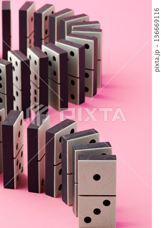 Dominoes setup on pink background ready for falling in a chain reaction event Dominoes setup on pink background ready for falling in a chain reaction event 136669116