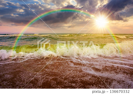 stormy weather on the sandy beach at sunset. dramatic sky over the sea in evening light. moody summer landscape. green waves crashing the shore. majestic cloudscape and rainbow above the horizon stormy weather on the sandy beach at sunset. dramatic sky over the sea in evening light. moody summer landscape. green waves crashing the shore. majestic cloudscape and rainbow above the horizon 136670332