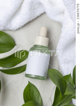 Glass dropper bottle near white bath towel and green leaves top view, skincare packaging mockup 136670779