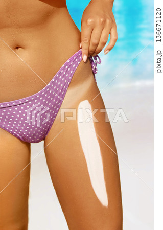 Woman applying sunscreen to legs. 136671120