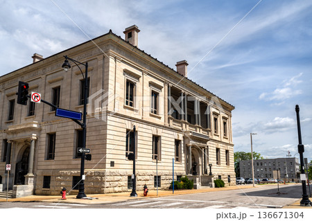 Former Kansas City Public Library building in Missouri. Historic Neoclassical architecture features massive stone blocks and ionic columns at a downtown street corner under a blue sky 136671304