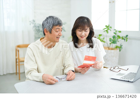 リビングで貯金通帳を見る60代の夫婦 リビングで貯金通帳を見る60代の夫婦 136671420