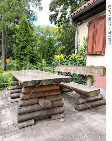 Rustic wooden garden table and bench made of logs against a backdrop of lush greenery 136671475