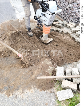 A worker compacts the soil with a vibrating plate A worker compacts the soil with a vibrating plate 136671478