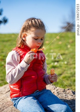 Little girl sitting on decorative stones blowing soap bubbles in city park. Spring childhood leisure and joyful outdoor play. 136672033