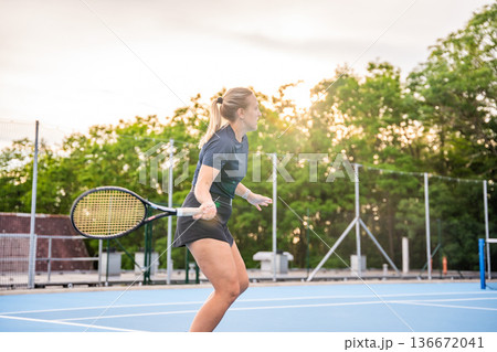 Professional female tennis player playing in tennis with racket and ball on outside court at sunset light 136672041