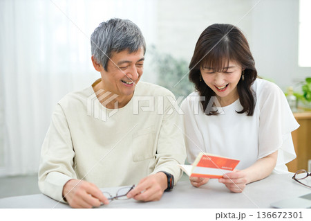 リビングで貯金通帳を見る60代の夫婦 136672301