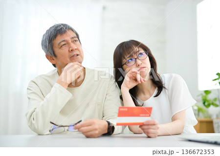 リビングで貯金通帳を見る60代の夫婦 リビングで貯金通帳を見る60代の夫婦 136672353