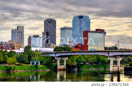 Little Rock skyline in Arkansas. Downtown city view features the Main Street Bridge with a yellow streetcar crossing the Arkansas River near Riverfront Park under a cloudy sky 136672368