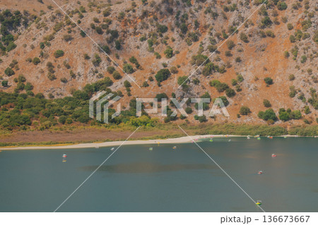 Drying mountain lake with wide strip of dried shore and orange rocky slope. 136673667