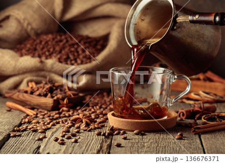 Black coffee is poured from a Turkish copper coffee pot into a glass cup. Black coffee is poured from a Turkish copper coffee pot into a glass cup. 136676371